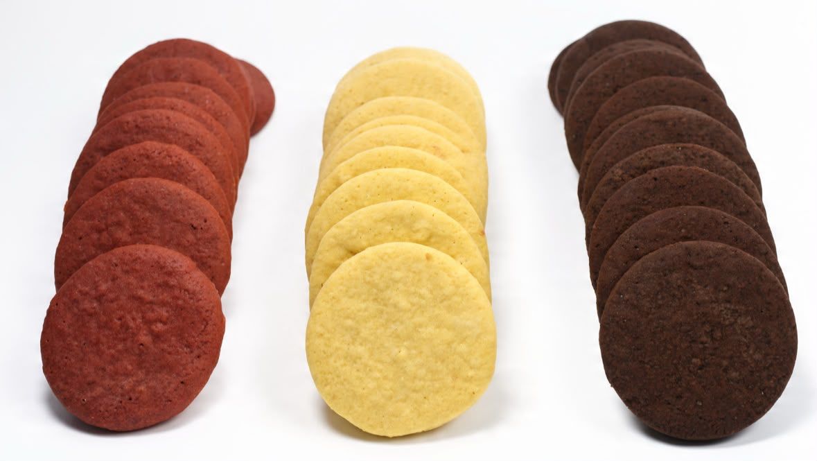 Tres filas de tapitas de Momento sin armar: unas rojizas, otras doradas y otras de cacao.
